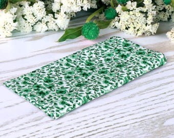 Può includere: Un tessuto bianco con un motivo floreale verde. Il tessuto è piegato a metà e si trova su una superficie di legno bianco.