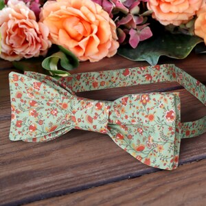 May include: A green bow tie with a floral pattern in shades of orange and red. The bow tie is made of fabric and has a classic bow shape.