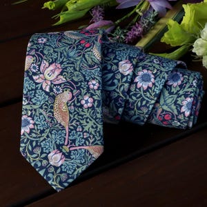 May include: A dark blue necktie with a floral pattern featuring pink flowers, green leaves, and brown birds. The pattern is reminiscent of vintage wallpaper.