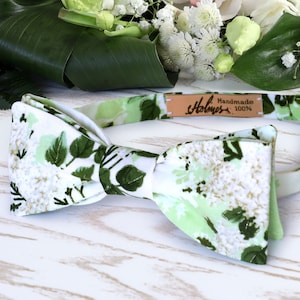 May include: A green and white floral bow tie with a brown leather label that reads "Holmes Handmade 100%".