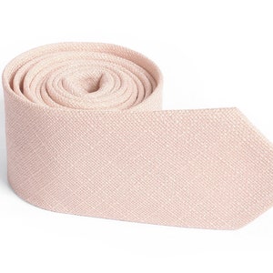 May include: A rolled-up, light pink necktie with a textured weave. The tie is made of a soft fabric and has a classic pointed end. The background is plain white, highlighting the tie's color and texture.