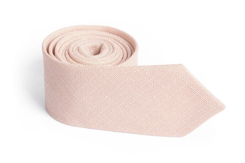 May include: A rolled-up, light pink necktie with a textured weave. The tie is made of a soft fabric and has a classic pointed end. The background is plain white, highlighting the tie's color and texture.