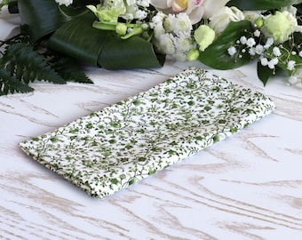 May include: A white fabric napkin with a green floral pattern. The napkin is folded and lying on a white wooden surface.