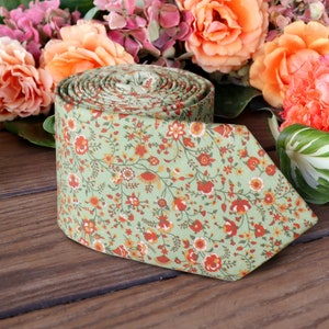 May include: A green necktie with a floral pattern featuring small orange, red, and white flowers. The tie is rolled up and lying on a wooden surface.