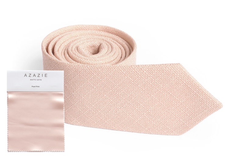 May include: A rolled-up, light pink matte satin tie with a matching swatch and packaging. The packaging reads "AZAZIE MATTE SATIN Pearl Pink". The tie is a solid color and has a textured appearance.