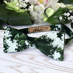 May include: A green bow tie with a white floral pattern. The bow tie has a brown leather label that says "Handmade Holmes 100%".