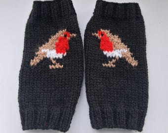 May include: A pair of charcoal gray knit fingerless gloves featuring a robin bird motif on each piece. The birds are depicted in shades of brown, white, and bright red, showcasing a detailed knitted texture with ribbed cuffs at the top and bottom.