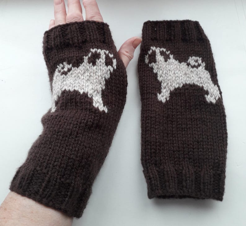 May include: A pair of brown knitted fingerless gloves with a white pug design. The gloves are made of a soft, warm material and are perfect for keeping your hands warm in the winter.