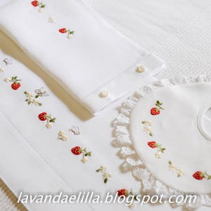 Puede incluir: Babero blanco de bebé bordado con ribete de encaje y diseño de fresas. El babero tiene un pequeño lazo en la parte superior para colgar.
