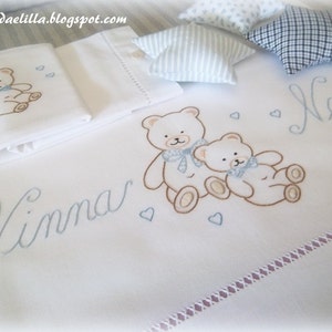 Può includere: Set di biancheria da letto per bambini bianco con orsetti ricamati, cuori e i nomi "Ninna" e "Nanna" in corsivo azzurro. Include piccoli cuscini decorativi. Il sito web "lavandaelilla.blogspot.com" è visibile.