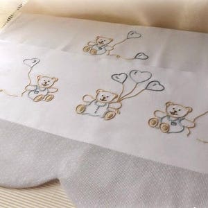 Può includere: Lenzuolo per culla bianco con bordo a festoni e orsacchiotti ricamati che tengono palloncini a forma di cuore. Gli orsacchiotti sono in tonalità di marrone e blu.