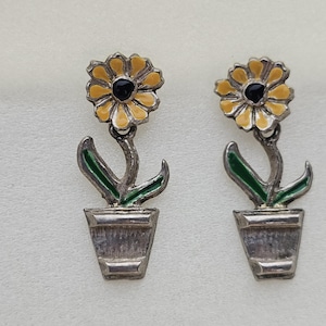 May include: A pair of silver earrings with yellow and green enamel flowers in pots. The flowers have black centers.