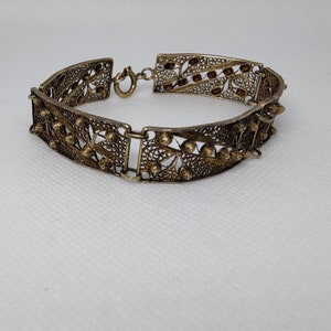 May include: A silver filigree bracelet with a floral design and a clasp closure.
