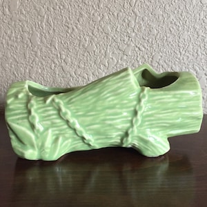 May include: A green ceramic planter shaped like a tree log. The planter has a rough texture and a chain design around the middle.