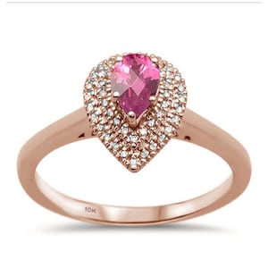 Könnte beinhalten: Roségoldener Ring mit einem birnenförmigen, rosa Edelstein, umgeben von kleinen, klaren Steinen. Der Ring hat ein schlichtes, poliertes Band. Auf der Innenseite ist "10K" eingraviert. Ein klassisches Schmuckstück.