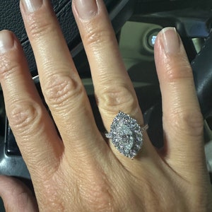 May include: A pear-shaped diamond engagement ring with a halo setting. The ring is set in white gold and features a large centre stone surrounded by smaller diamonds.