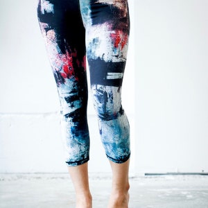 May include: A pair of black leggings with a colorful abstract print in shades of blue, red, and white. The leggings are cropped and have a high waist.