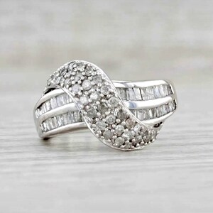 Könnte beinhalten: Ein silberner Ring mit wellenförmigem Design, besetzt mit kleinen runden Diamanten und größeren Baguette-Diamanten.