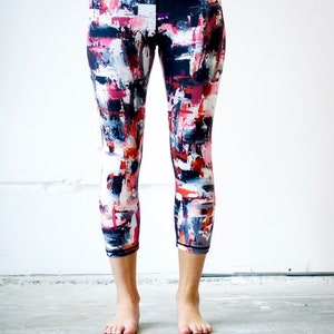 May include: A pair of black leggings with a colorful abstract print featuring shades of pink, white, and blue. The leggings are cropped and have a high waist.