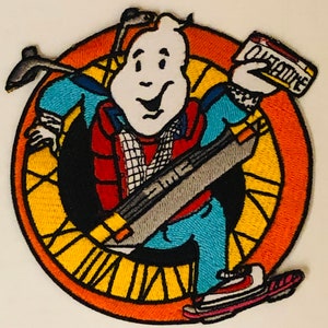 May include: A round embroidered patch featuring a cartoon ghost wearing a red vest, blue jeans, and a grey backpack. The ghost is holding a white box with the word "OUTATIME" printed on it. The patch is surrounded by a yellow and orange circle with a clock face design.