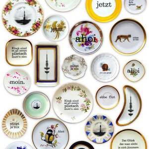 K&ouml;nnte beinhalten: Eine Sammlung von 20 dekorativen Tellern mit verschiedenen Designs und Spr&uuml;chen. Die Teller sind wei&szlig; mit goldenen Verzierungen und zeigen eine Vielzahl von Bildern, darunter Tiere, Blumen und Text. Die Teller sind in einem Rastermuster auf wei&szlig;em Hintergrund angeordnet.