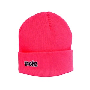 Op de afbeelding: Een felroze beanie met een zwart geborduurd "mo'm" logo.