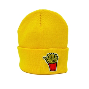 Op de afbeelding: Een gele gebreide beanie met een rode en gele frietjes afbeelding.