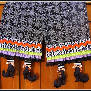 May include: Black and white fabric with a spiderweb pattern, trimmed with black, white, orange, and green ruffled fabric. Four black witch's boots with orange bows hang from the bottom.