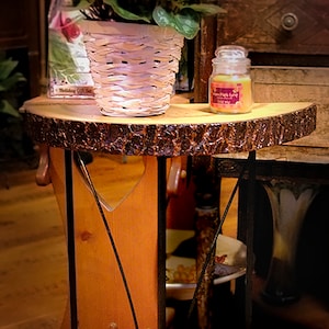 May include: A rustic side table with a wood top and a black metal base. The table has a curved top and a unique design with three metal supports. The table is sitting on a wooden floor.