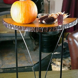 May include: A wooden table with a live edge top and black metal legs. The table is decorated with a pumpkin, corn husks, and a red candle.
