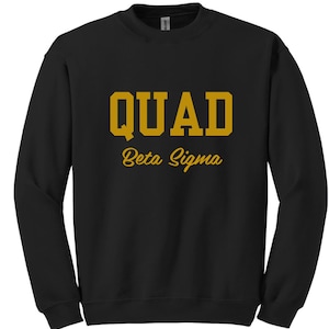 May include: Black crewneck sweatshirt with the word "QUAD" in gold block letters above the words "Beta Sigma" in gold script. The sweatshirt is a solid black color.