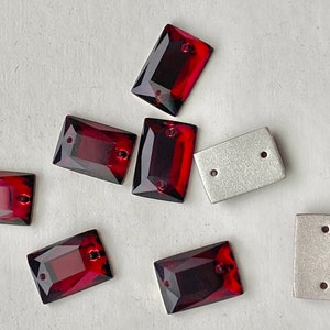 May include: Rectangular, faceted, dark red glass beads with two holes for stringing, alongside two silver-colored metal rectangles with two holes each. The beads have a polished, reflective surface, and the metal pieces have a matte finish.