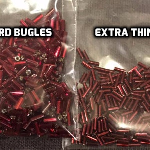 May include: Two clear plastic bags filled with red bugle beads. One bag is labeled "STANDARD BUGLES" and the other is labeled "EXTRA THIN BUGLES". The beads are cylindrical and appear to be made of glass or plastic, suitable for crafts.