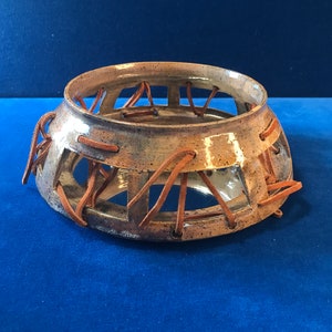 Könnte beinhalten: Eine Keramikschale mit brauner Glasur und einem geflochtenen Lederdesign. Die Schale hat eine runde Form und eine breite Öffnung.