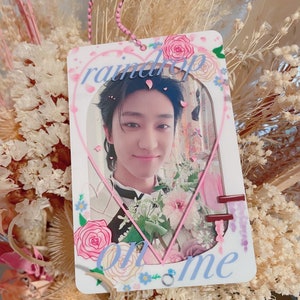May include: A white heart-shaped photo card with a pink border and floral accents. The card features a photo of a young man with dark hair and a light blue shirt. The text "raindrop on me" is written in blue letters on the card.