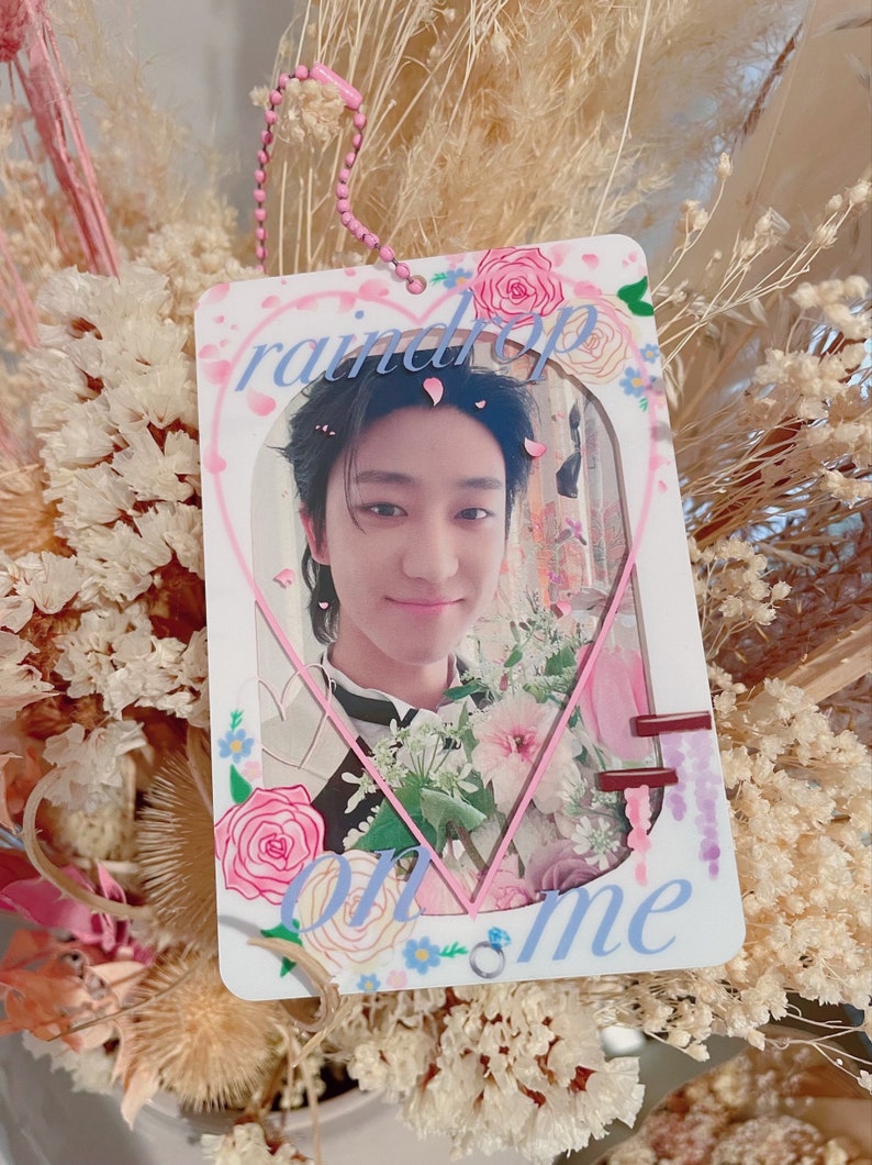May include: A white heart-shaped photo card with a pink border and floral accents. The card features a photo of a young man with dark hair and a light blue shirt. The text "raindrop on me" is written in blue letters on the card.