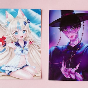 May include: Two anime-style art prints. One features a girl with fox ears and a crab on a beach. The other depicts a man in a black hat and purple clothing with a stylized face. The background is a light pink.