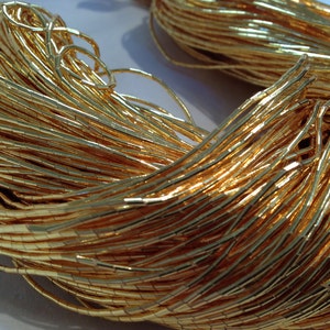 May include: A spool of gold-colored metallic beads. The beads are small and rectangular, and they are strung together in a long strand.