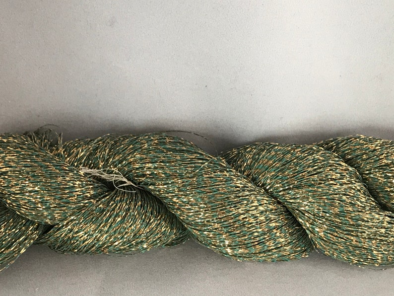 May include: A skein of green and gold metallic yarn. The yarn is made of a fine, shimmering thread that is perfect for creating delicate and elegant projects.