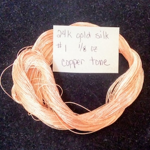 May include: A spool of 24K gold silk thread in a copper tone. The spool is labeled "24K gold silk #1 1/8 oz copper tone".