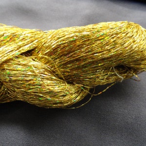 May include: A spool of gold metallic yarn with iridescent shimmer. The yarn is twisted and piled together.