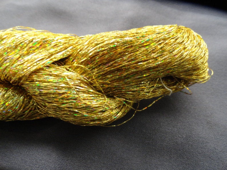 May include: A spool of gold metallic yarn with iridescent shimmer. The yarn is twisted and piled together.
