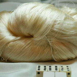 May include: A large bundle of off-white silk thread, resembling a fluffy cloud, is displayed on a white surface.  Five white dice with black dots are in the foreground.
