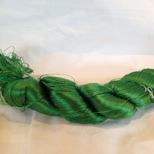Pode incluir: Uma meada de fio de seda verde brilhante, torcido e pronto para usar em projetos de artesanato ou bordado.