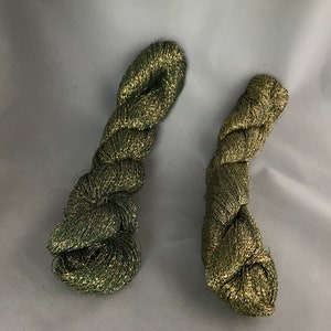 May include: Two skeins of green and gold metallic yarn. The yarn is twisted and has a shiny finish.