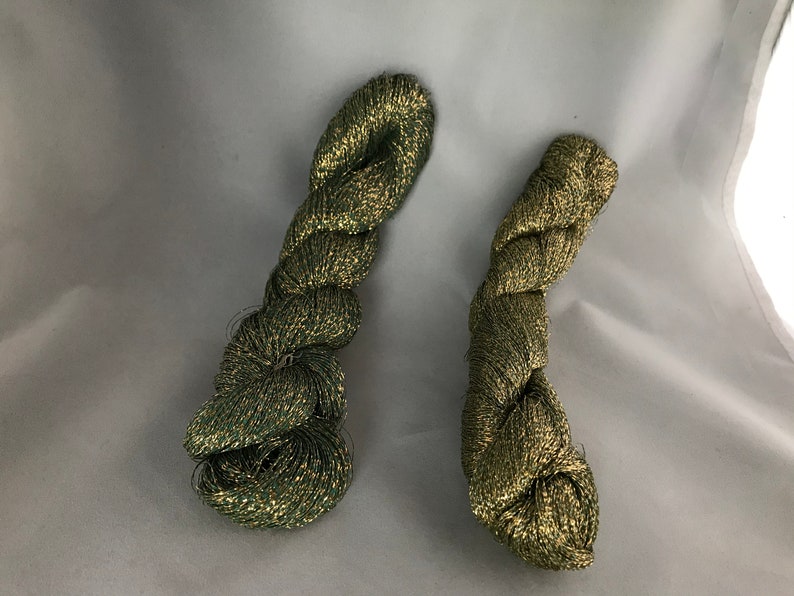 May include: Two skeins of green and gold metallic yarn. The yarn is twisted and has a shiny finish.