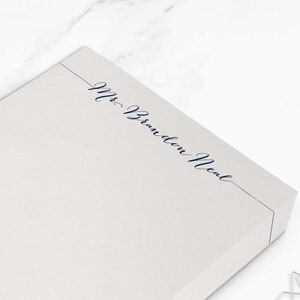Puede incluir: Bloc de notas rectangular crema. La esquina superior derecha presenta el texto "Mr. Branden Neal" en azul marino. Dos clips plateados están junto al bloc de notas. El bloc de notas mide aproximadamente 10,8 x 15,9 cm.