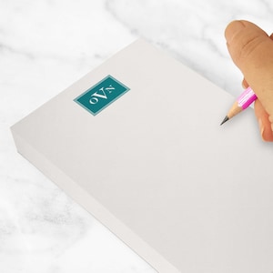 May include: A white notepad with a teal logo that reads "oVn". A pink pencil is held over the notepad, ready to write. The notepad is approximately 12.7 x 17.8 cm.