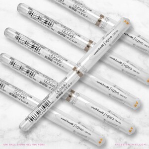May include: Several white Uni-ball Signo UM-153 gel ink pens are displayed. Each pen features a clear barrel, white body, and a cap with Japanese text. The pens are arranged on a light surface. The text "UNI BALL SIGNO GEL INK PENS" is at the bottom.