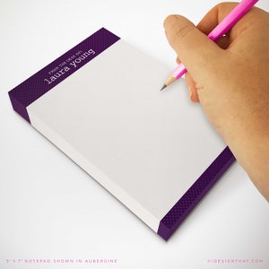 May include: A white notepad with a purple border and the text "FROM THE DESK OF: laura young" on the top. The notepad is 12.7 cm by 17.8 cm and is shown in the colour aubergine.